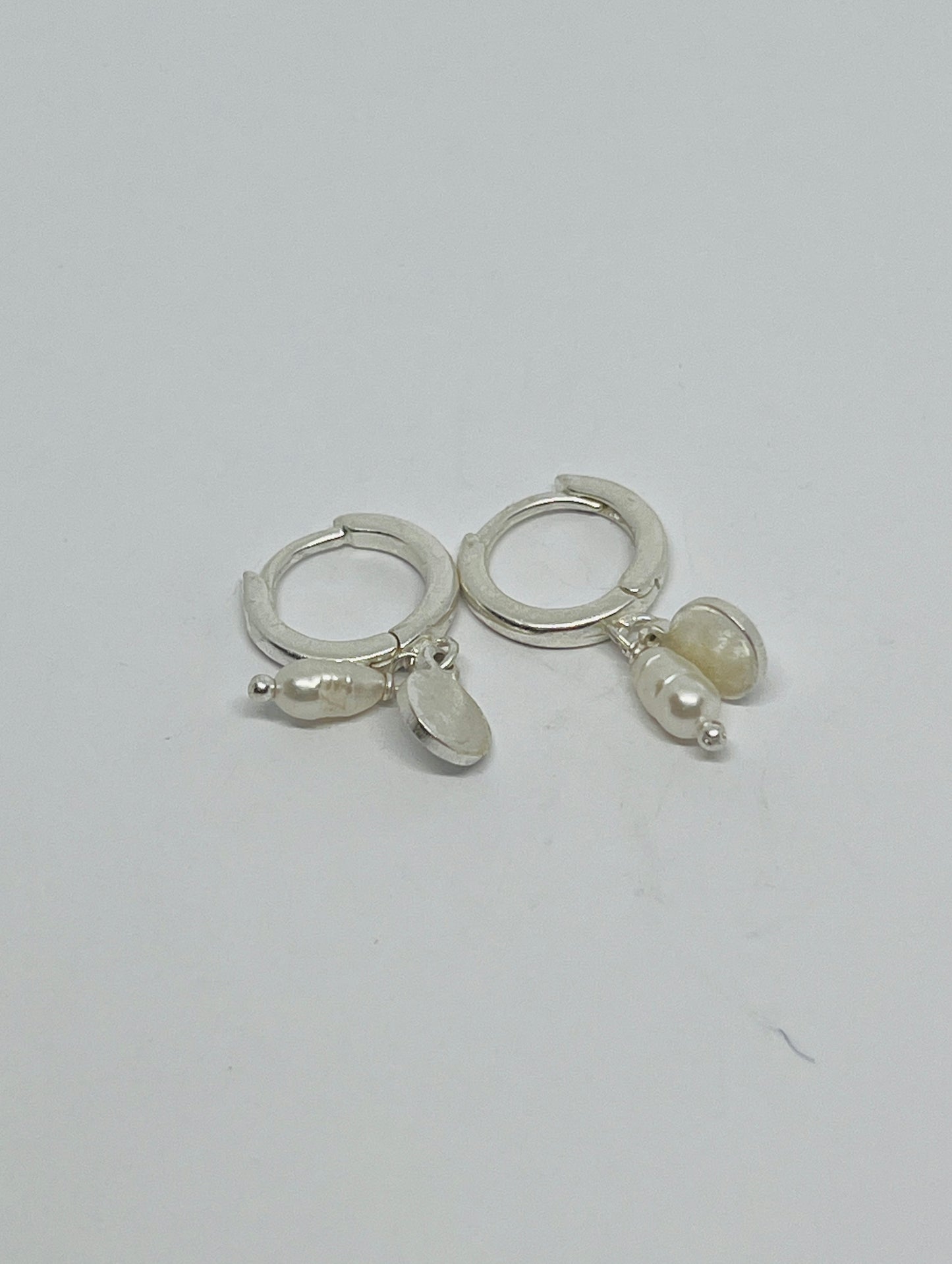 Silver hoop earrings with pearl-like charms on a light gray background