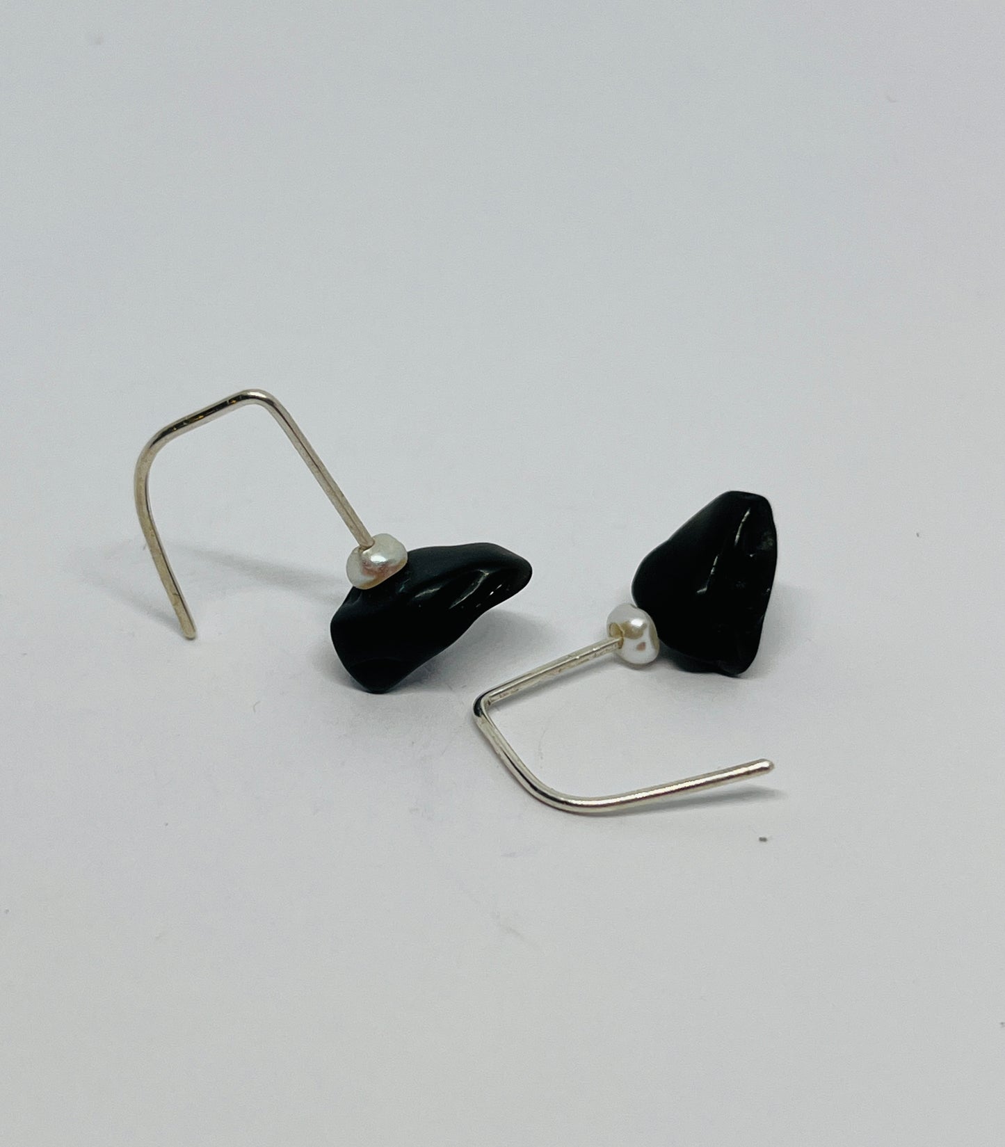Black teardrop and small pearl earrings with silver hooks on a light gray background