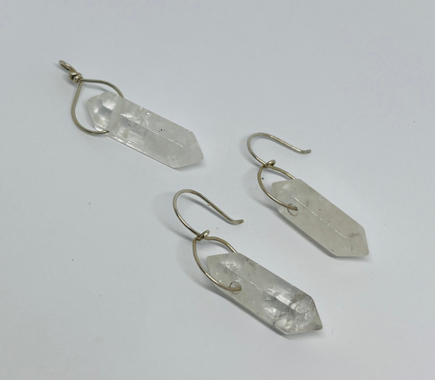 This stunning pair of dangling quartz earrings, paired with a matching pendant, embodies elegance and simplicity, creating a harmonious synergy that enhances your natural beauty. Each piece features exquisite quartz crystals, expertly wrapped in fine silver, showcasing their ethereal charm.
