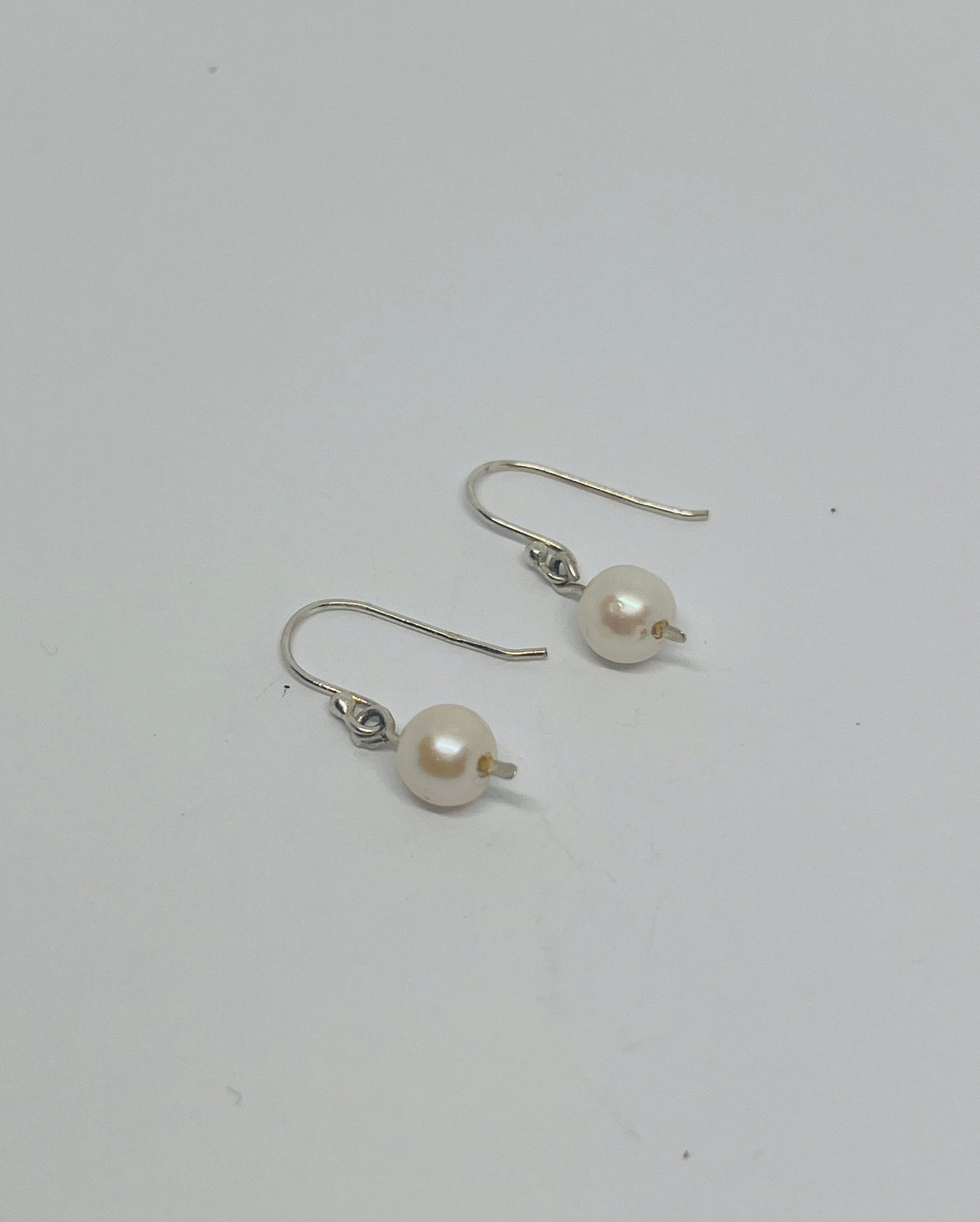 These enchanting dangle earrings feature classic white pearls, swaying gently with every movement and capturing the delicate interplay of light and shadow. Suspended from an elegant pressed post, they evoke a sense of understated grace.