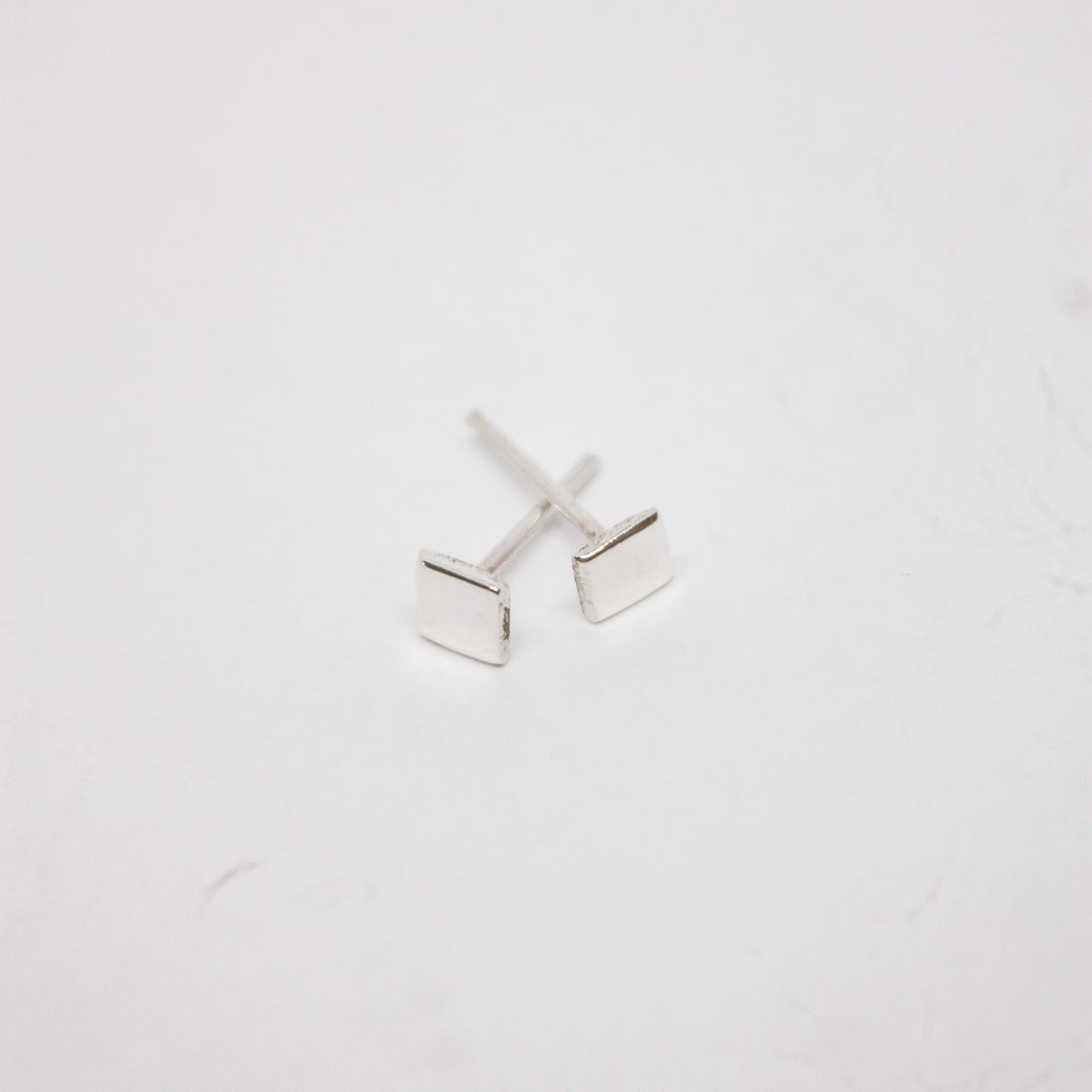 A pair of silver square stud earrings on a white background.