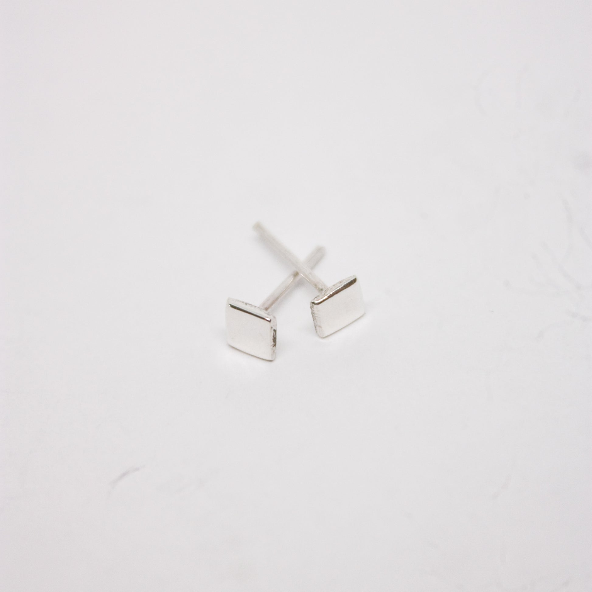 A pair of silver square stud earrings on a white background.