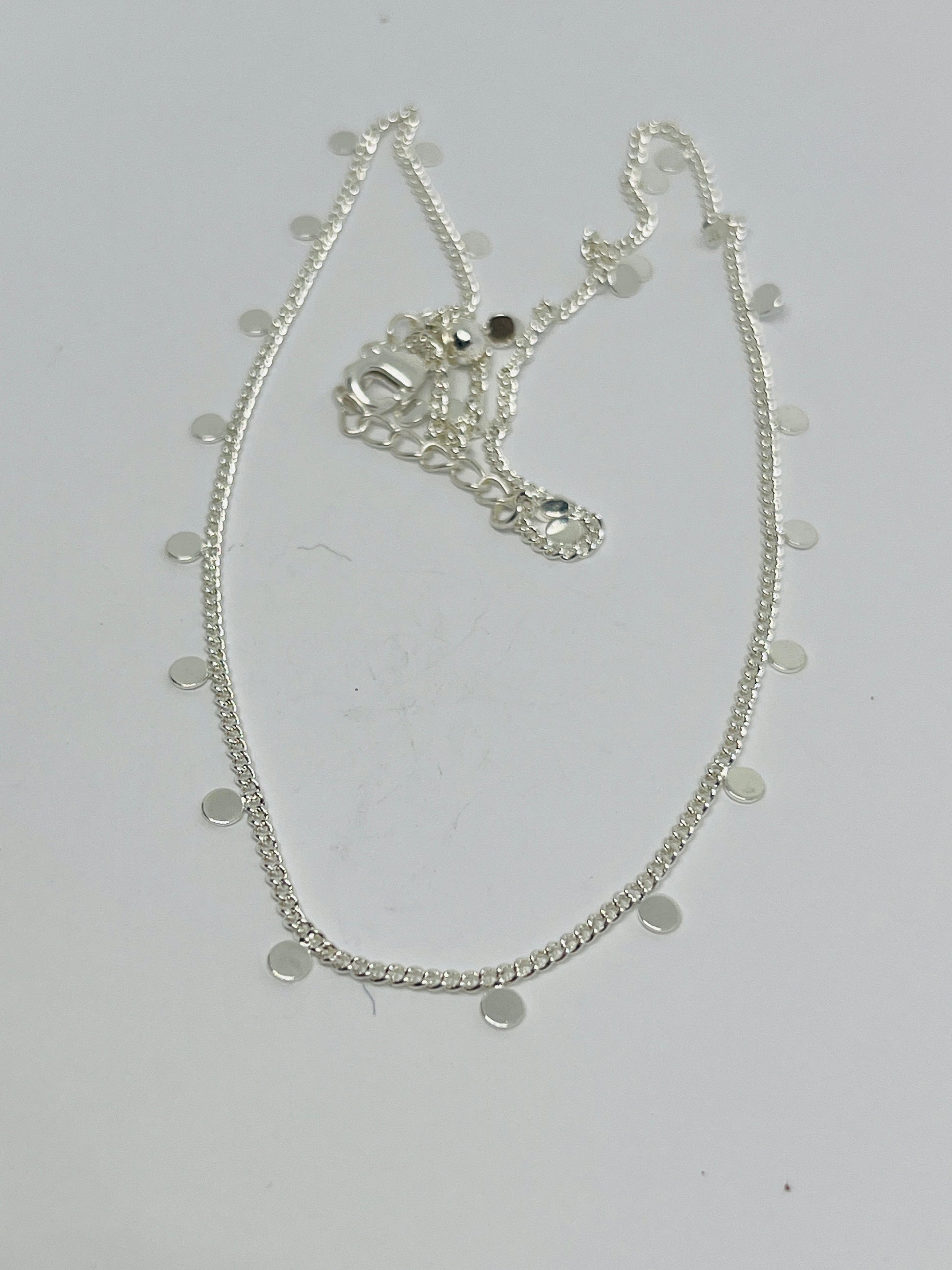 Silver necklace with circular pendants on a light gray background