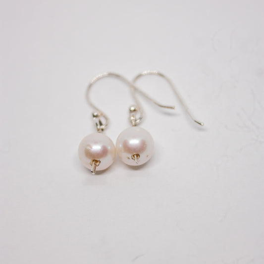 A pair of silver and white pearl dangle earrings laid out on a white surface.