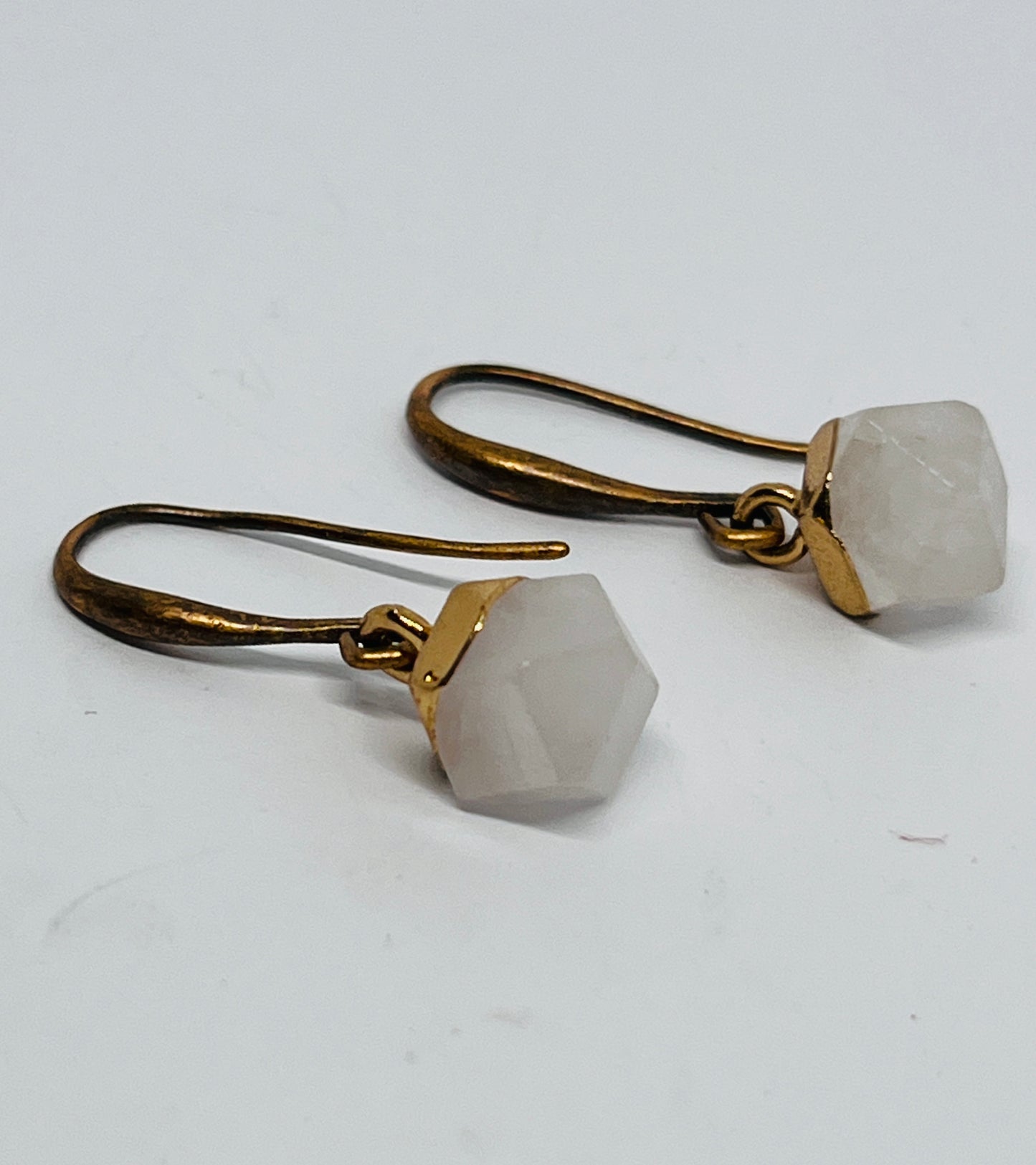 Pair of earrings with gold hooks and hexagonal stone beads on a light gray background