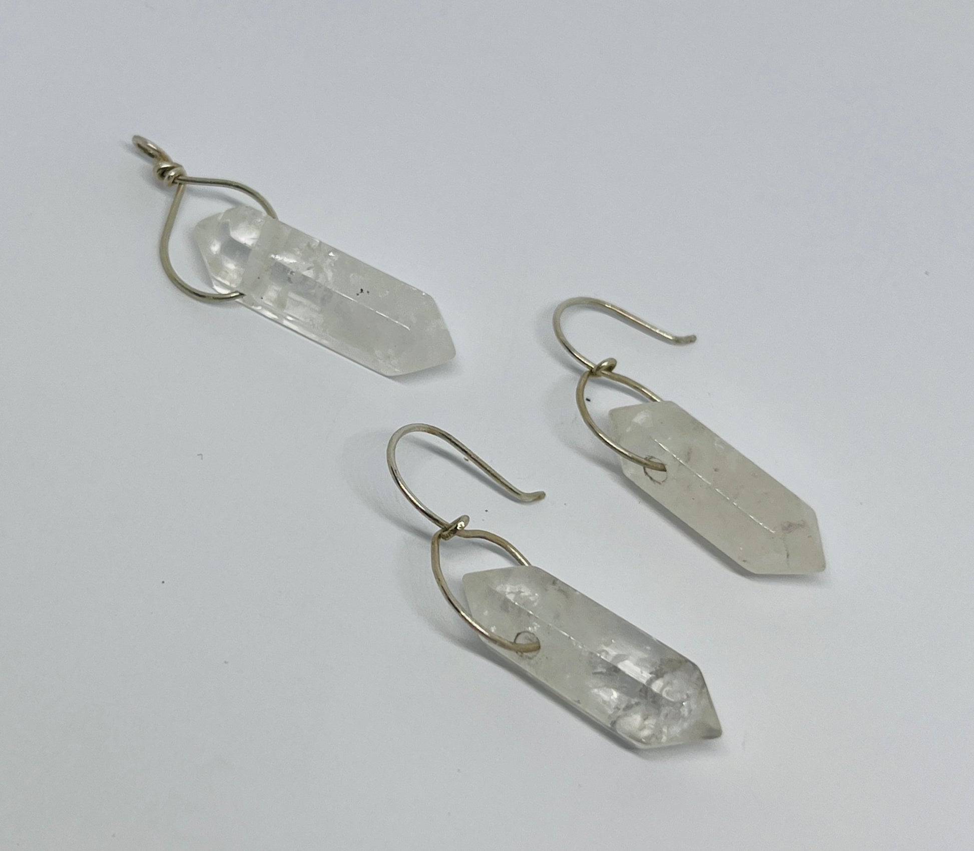 This stunning pair of dangling quartz earrings, paired with a matching pendant, embodies elegance and simplicity, creating a harmonious synergy that enhances your natural beauty. Each piece features exquisite quartz crystals, expertly wrapped in fine silver, showcasing their ethereal charm.