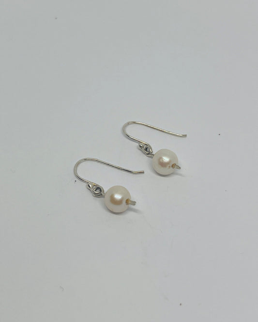 These enchanting dangle earrings feature classic white pearls, swaying gently with every movement and capturing the delicate interplay of light and shadow. Suspended from an elegant pressed post, they evoke a sense of understated grace.