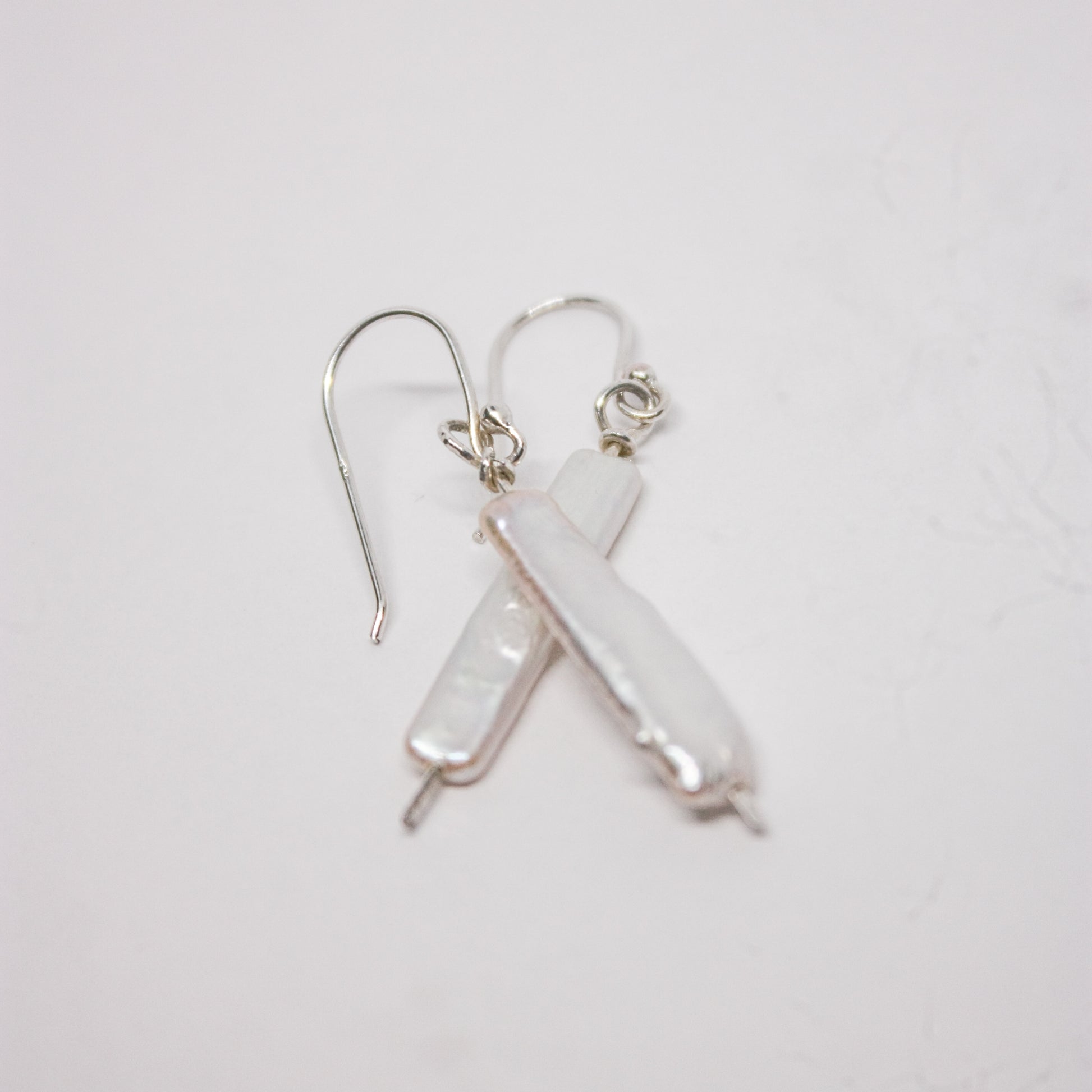 A pair of silver earrings with long baroque white pearls, laid out on a white surface.