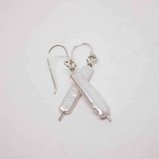 A pair of silver earrings with long baroque white pearls, laid out on a white surface.