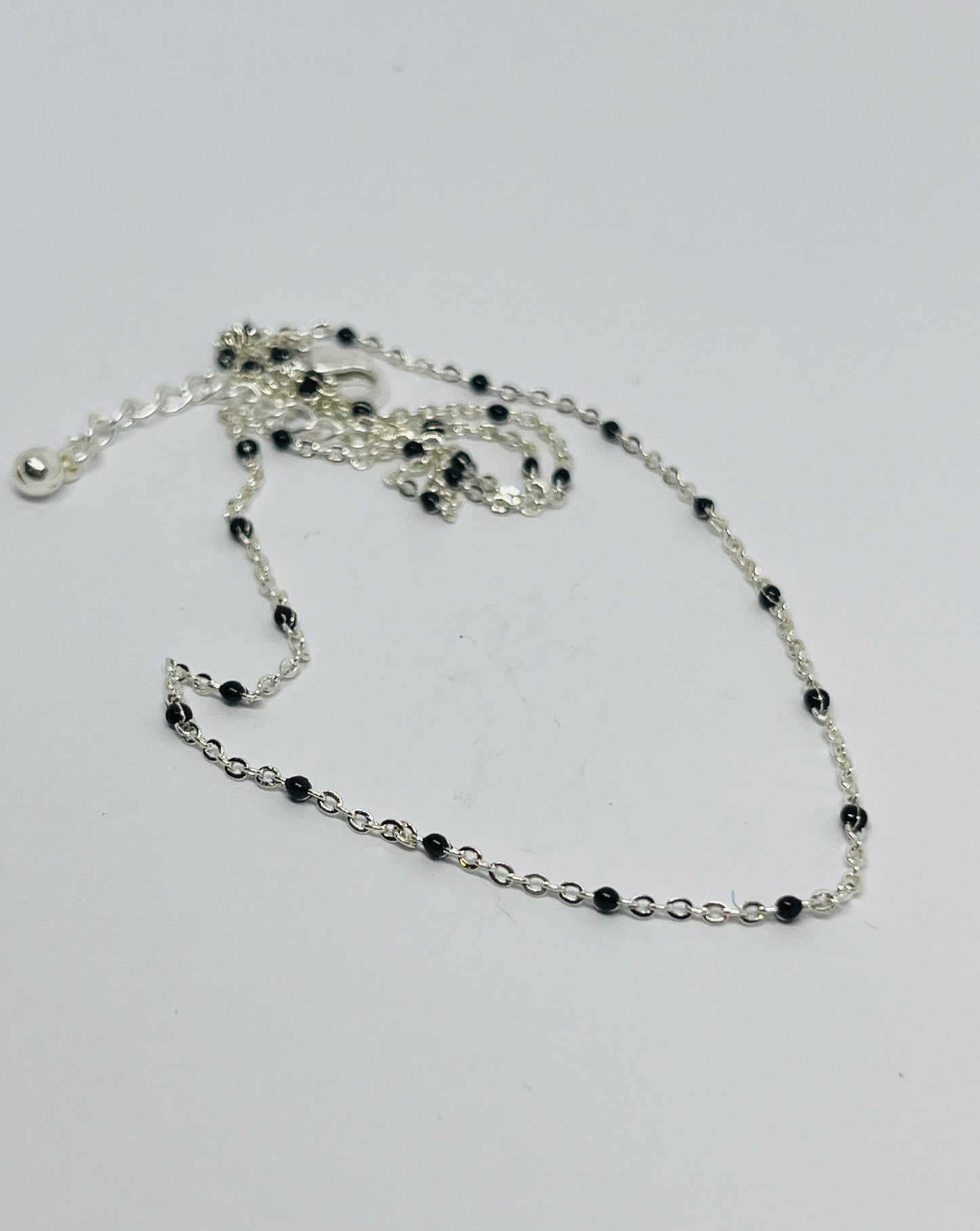Silver chain necklace with black beads on a white background