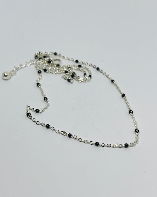 Silver chain necklace with black beads on a white background