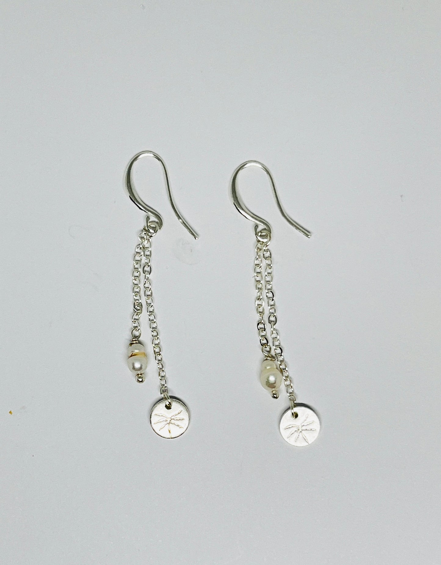 Pair of silver earrings with chain drops on a light gray background