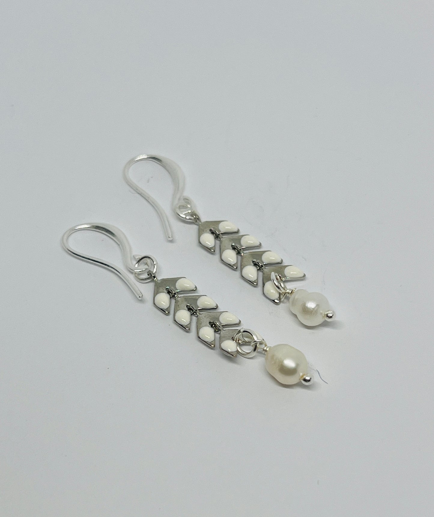 Silver earrings with white beads on a gray background