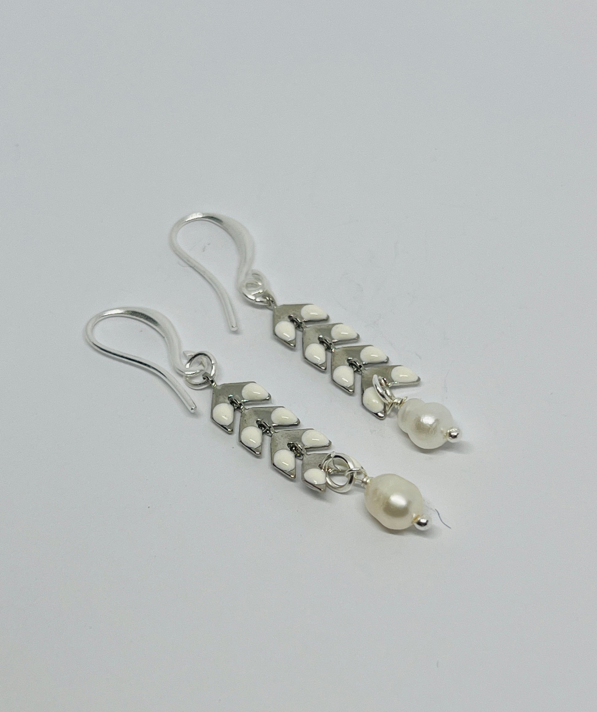 Silver earrings with white beads on a gray background